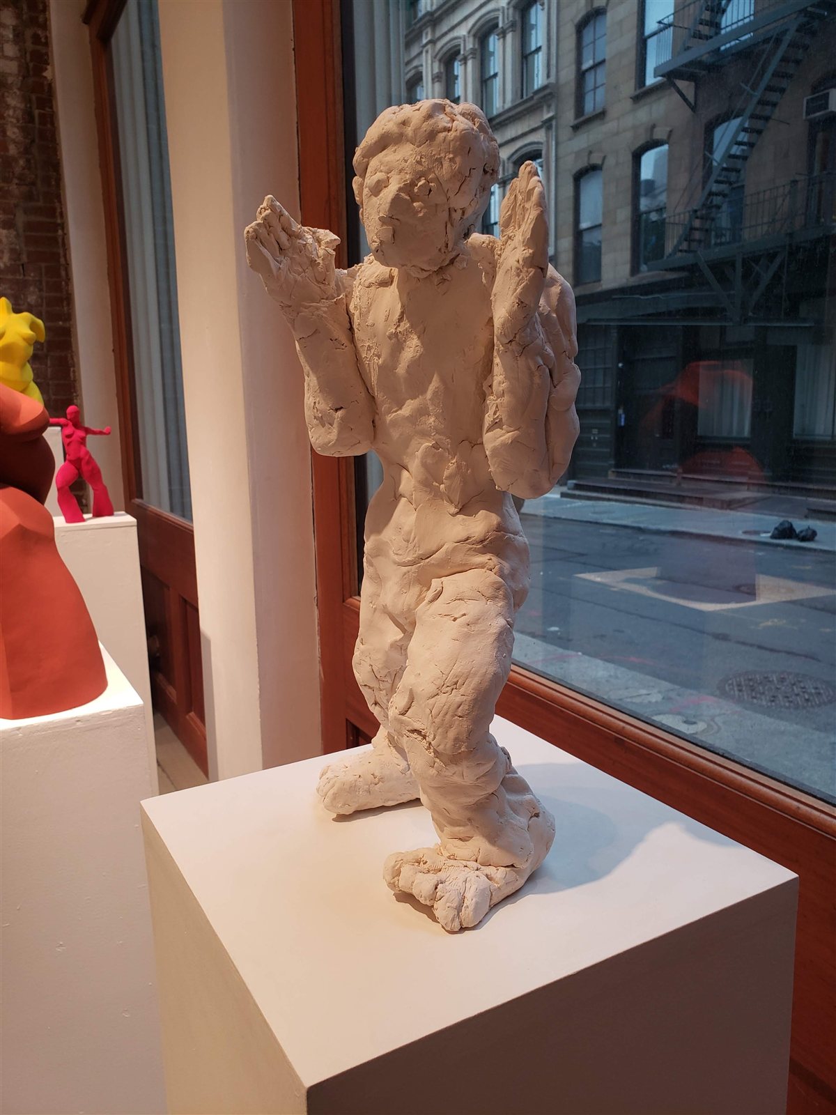 Cara de Pancake, clay sculpture of a standing figure with raised hands, seen from the left